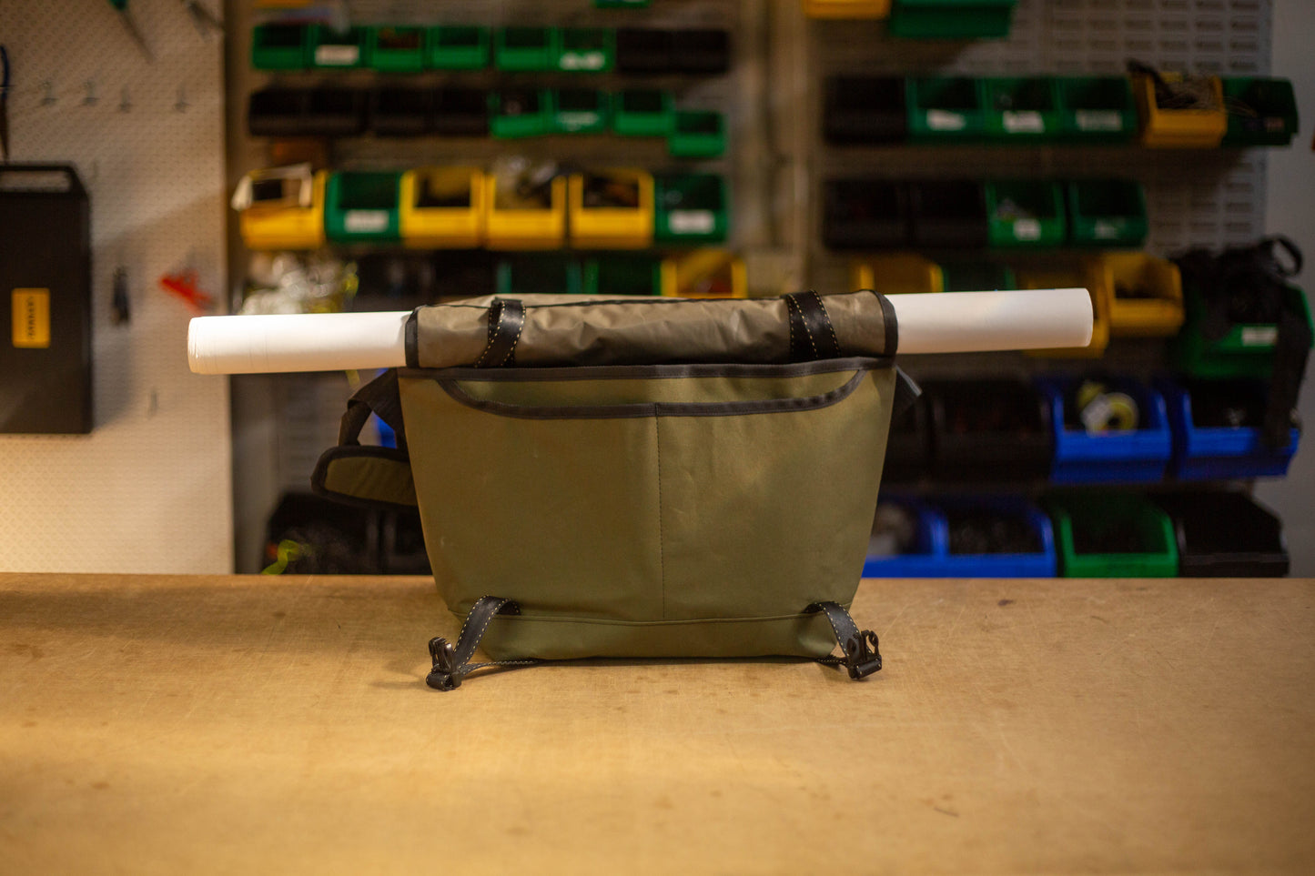 wipwrk Mondo Hauler messenger bag in green with top flap rolled up and integrated straps securing a rolled document tube, highlighting its hauling functionality