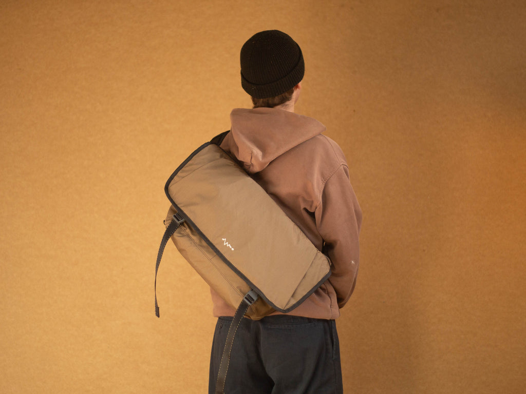 rear view of person wearing brown wipwrk Mondo messenger bag in green slung across the body with adjustable padded shoulder strap demonstrating on-body fit