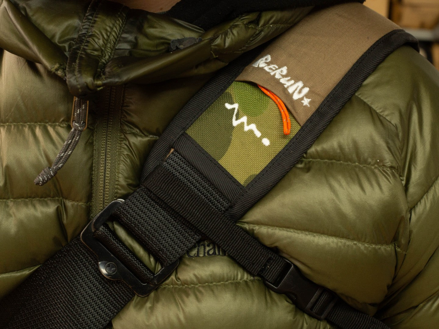 Close-up of person wearing wipwrk Mondo messenger bag showing tri-strap harness with adjustable padded shoulder strap, camo logo pad, and quick-release sternum buckle